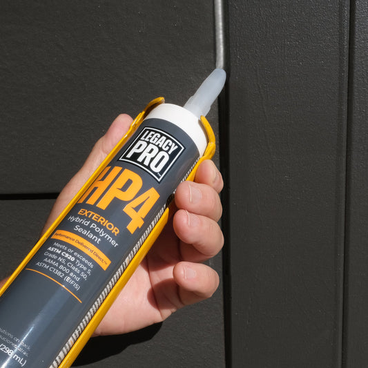 Caulk gun with tube of Legacy Pro HP4 applying exterior sealant against dark siding.
